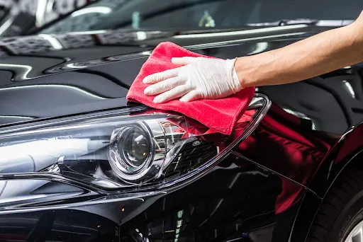 a black car's headlight being cleaned by a red fabric